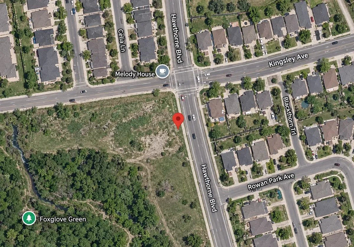 Aerial view of the vacant corner site, with built townhouse rows across Kingsley Avenue to the north, a detached subdivision across Hawthorne Boulevard to the east, and wooded valley land to the southwest.